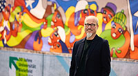 Bild: Protest movements in Latin America reach as far as Bielefeld: historian Olaf Kaltmeier in front of a reproduction of the Chile mural in the university’s mainhall. At present