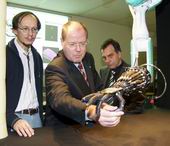 Bild: Buz 218/2004 - Ministerpräsident Steinbrück im Griff der von Wissenschaftlern der Technischen Fakultät entwickelten Roboter-Hand. Helge Ritter (l.) und Gerhard Sagerer (r.) verfolgen gespannt die mit "Bewegungsintelligenz" ausgestattete Roboter-Hand.
