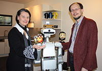 Bild: Prof. Dr.-Ing. Britta Wrede und Prof. Dr. Helge Ritter begrüßen den Roboter der Firma Meka Robotics. Der neue Service-Roboter soll mit einer Variante des Flobi-Kopfes (Hintergrund) ausgestattet werden. Foto: Universität Bielefeld