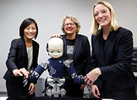 Bild: Prof. Yukie Nagai PhD von der Universität Osaka (l.) präsentiert Wissenschaftsministerin Svenja Schulze (Mitte) und Prof. Dr. Friederike Eyssel den kindgroßen Roboter iCub im Emergent Robotics Lab. Foto: Ina Fassbender
